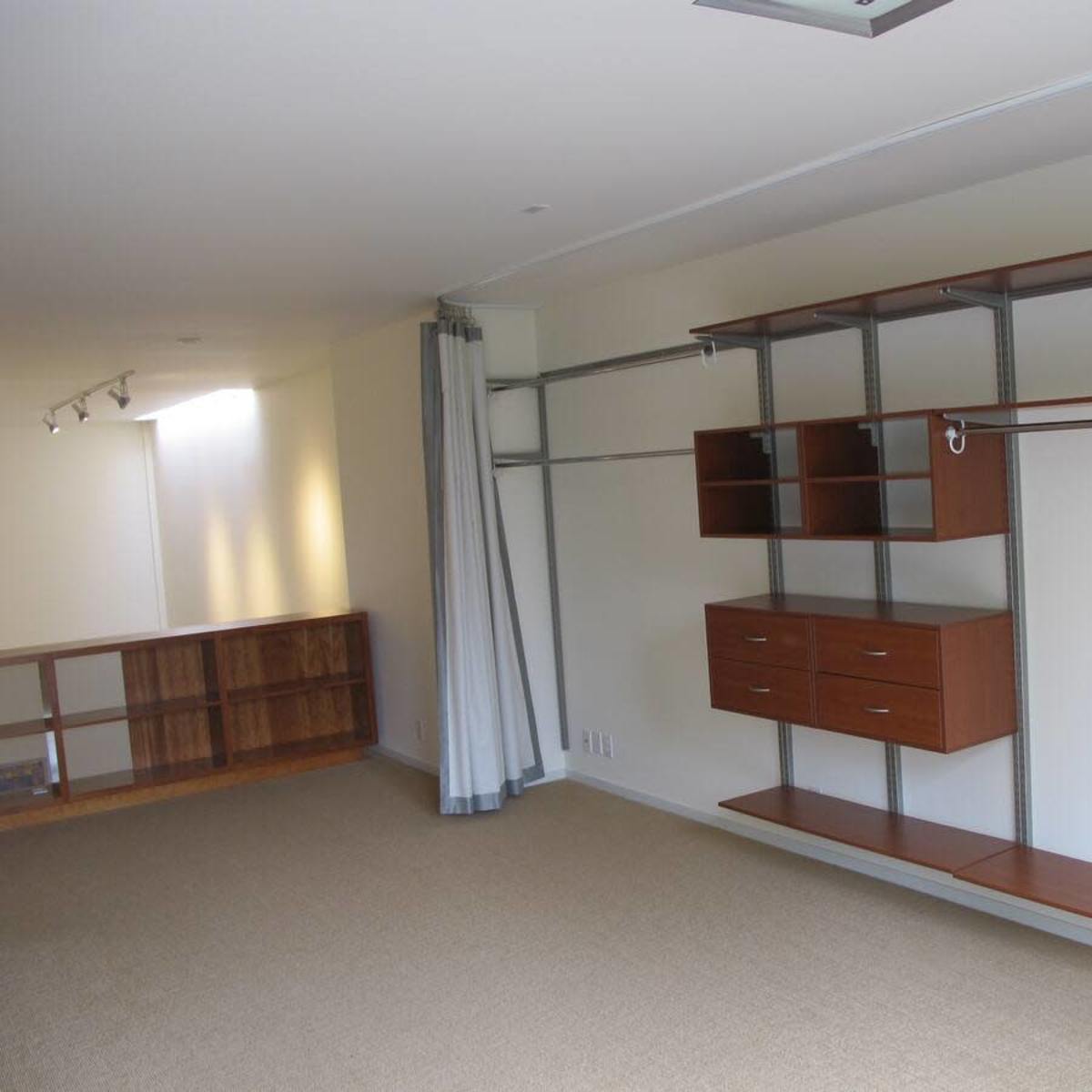 A minimalist closet space with wooden shelves, drawers, and a curtain along one side, all set against a light-colored wall.