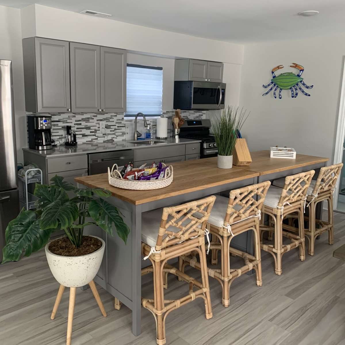 A modern kitchen features gray cabinets, stainless steel appliances, a wooden island with seating, and a decorative crab wall art.