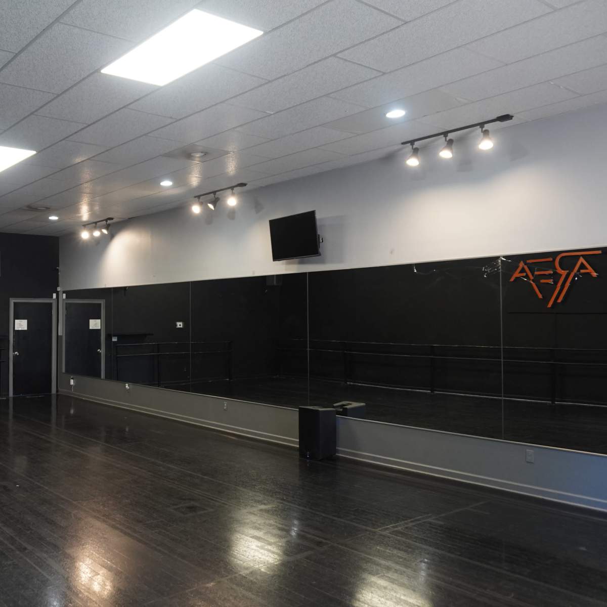 An empty dance studio with a wooden floor, mirrored wall, and overhead lights.