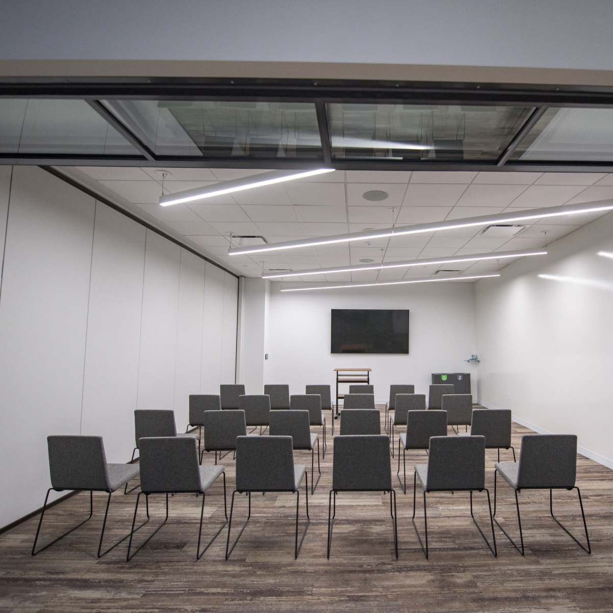 A modern conference room features rows of gray chairs facing a wall-mounted screen.