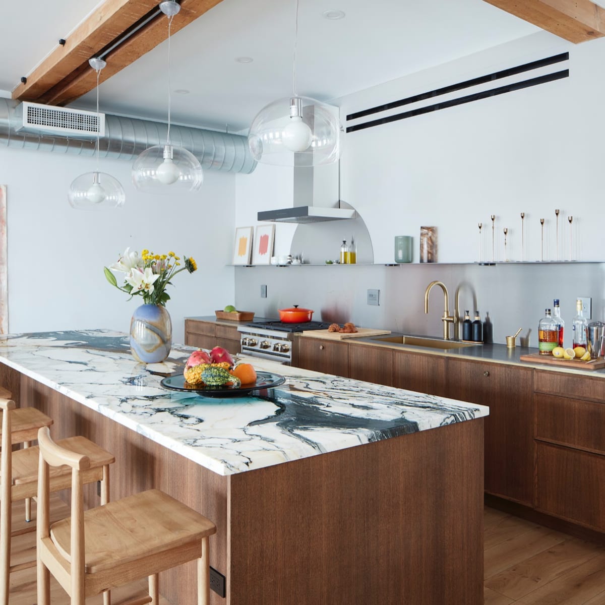 A modern kitchen features a wooden island with a marble countertop, stainless steel appliances, and light wood bar stools.