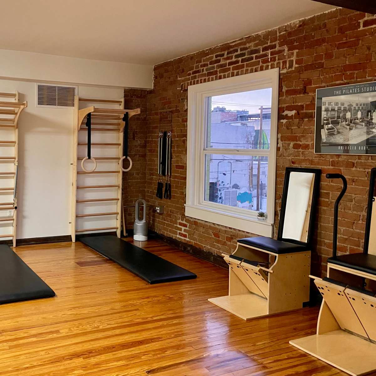 A minimalist Pilates studio featuring wooden equipment, mirrors, and exposed brick walls.