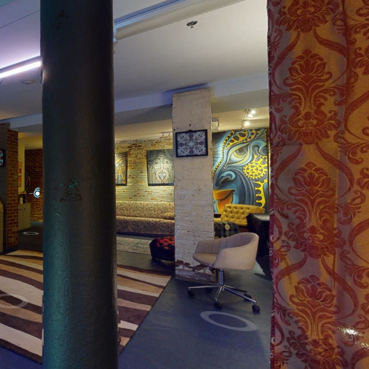 A spacious room with musical instruments, a decorative rug, and various artworks on the walls, separated by columns and curtains.