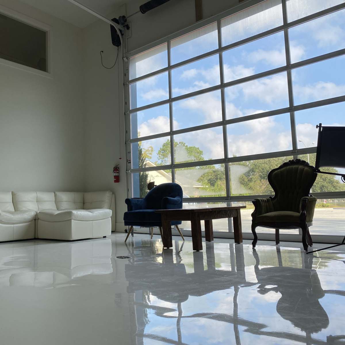A modern interior with a white sectional sofa, two distinct chairs, and a wooden table, all situated on a glossy floor beside large glass windows.