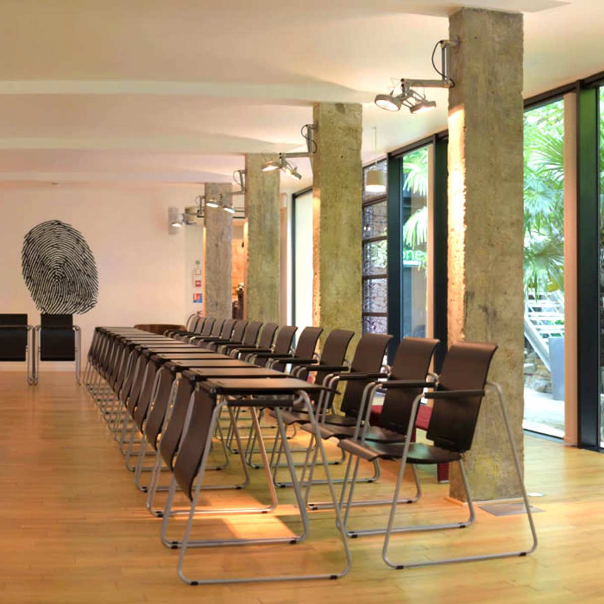 A modern conference room arranged with rows of chairs facing a presentation screen and an artistic fingerprint design on the wall.