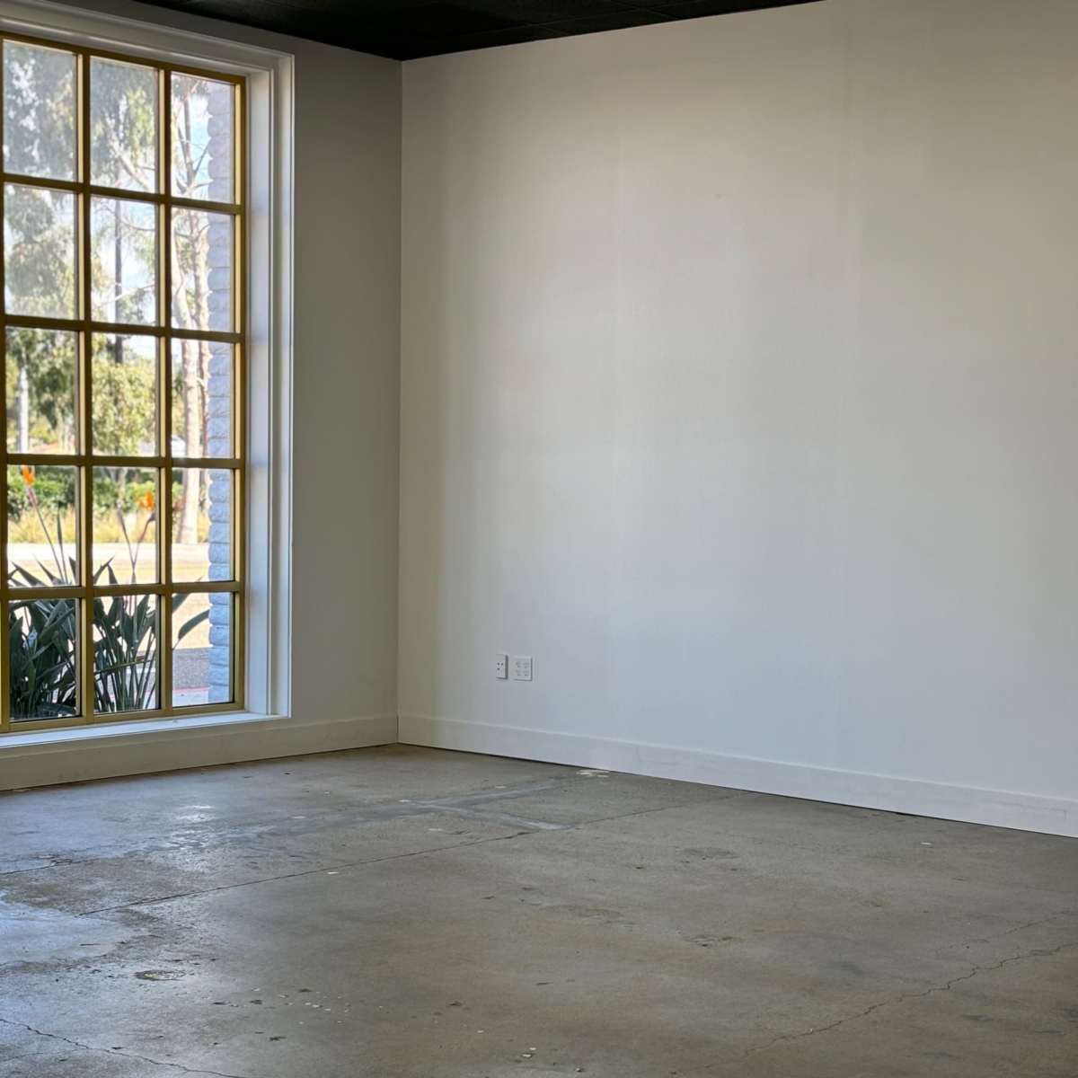 An empty room with a concrete floor and a large window letting in natural light.