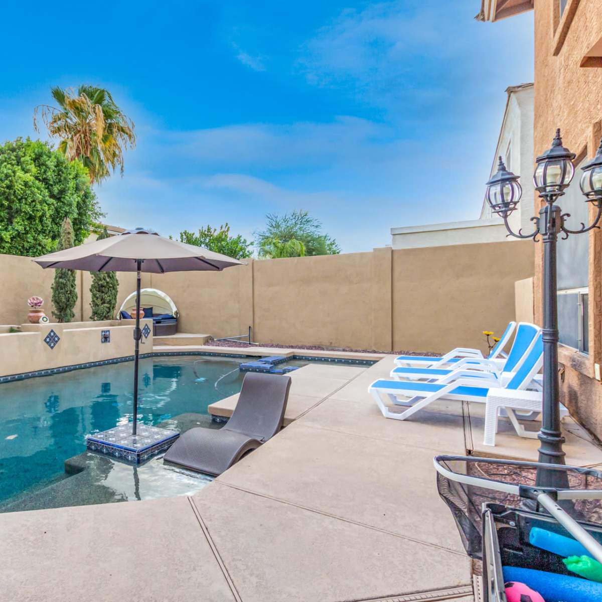 A backyard pool area with an umbrella, lounge chairs, and a surrounding wall.