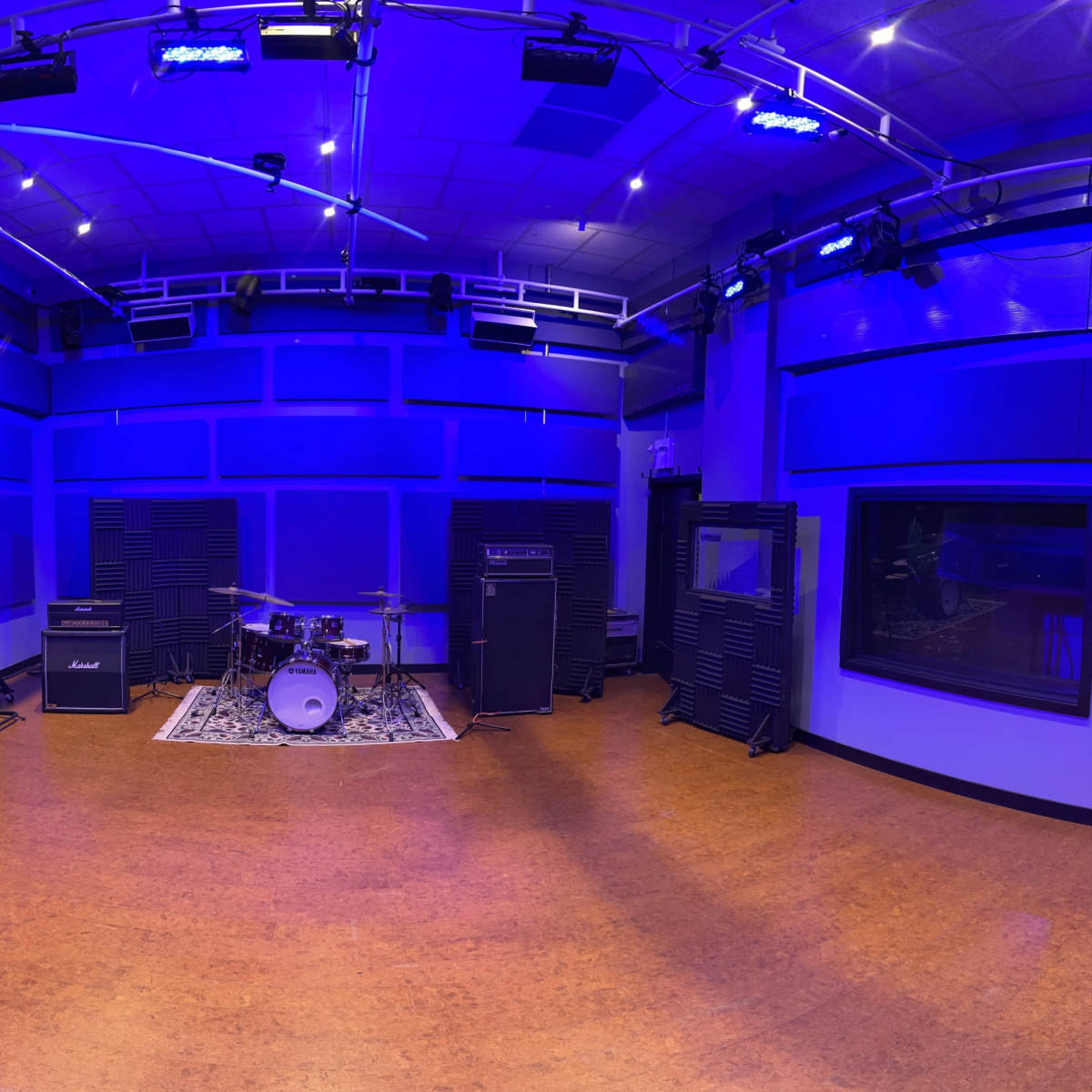 A music studio with a drum set and amplifiers arranged against blue-lit walls.