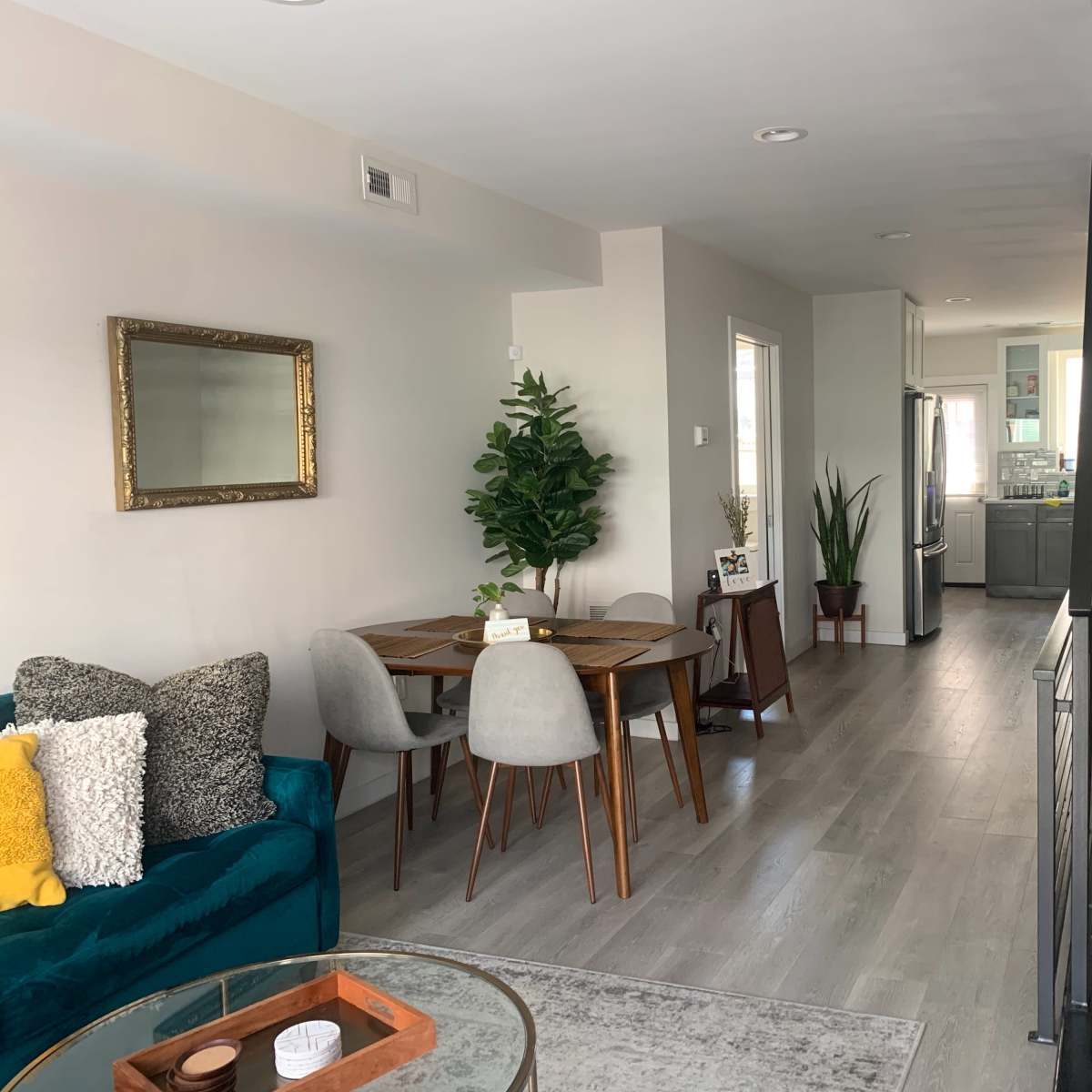 A modern, open-concept living space featuring a dining area with a wooden table, a green couch, and a staircase in the background.