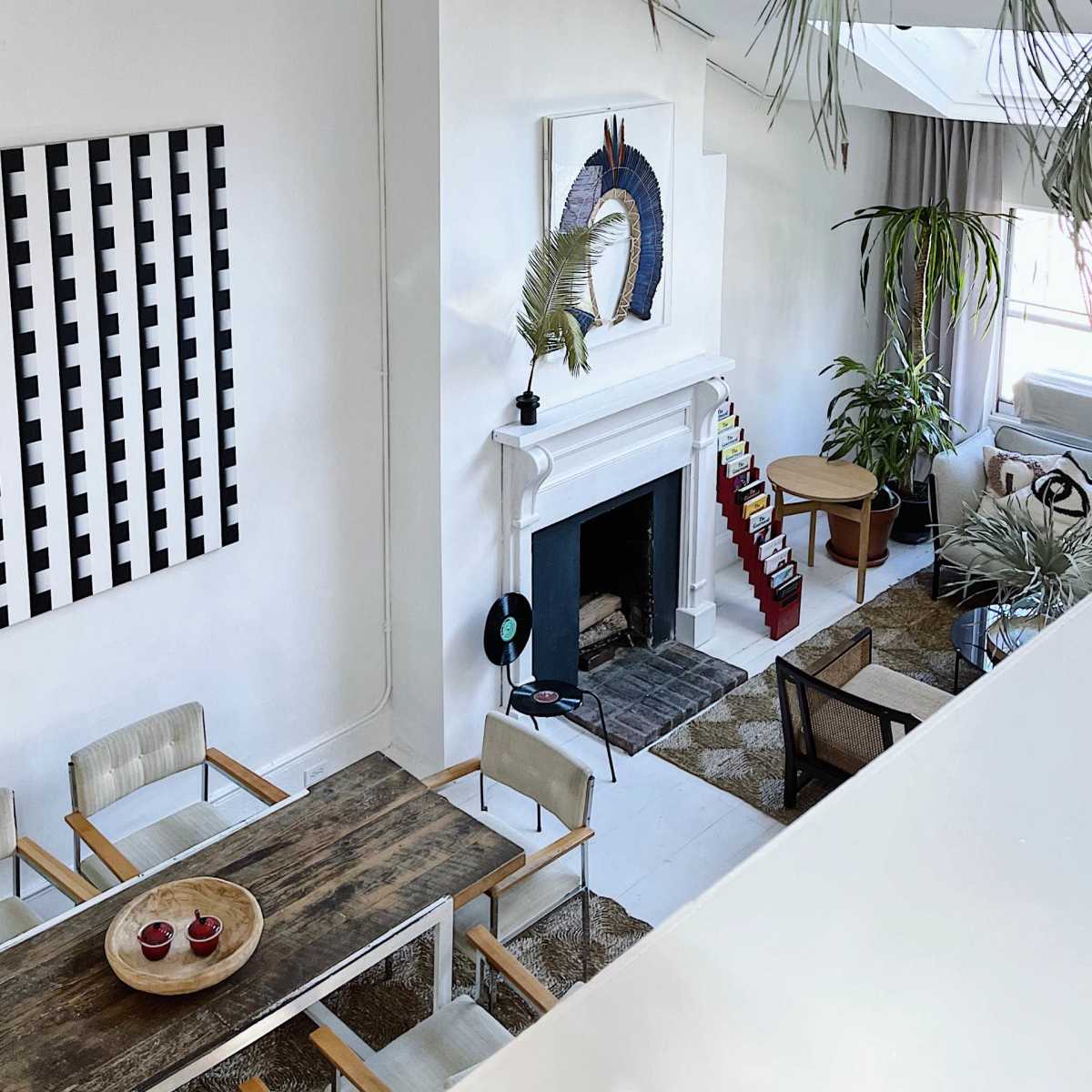A modern living room with a white fireplace, a dining table, and large plants, accented by a geometric wall art piece.