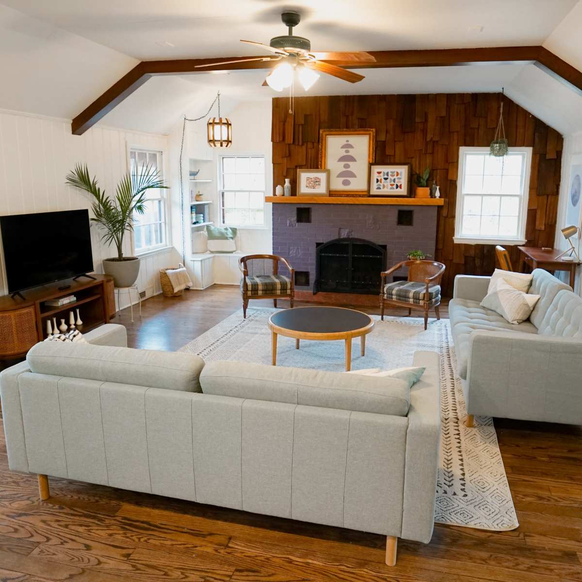 A spacious living room features a light blue sofa and a circular coffee table, with a television and a fireplace in view.