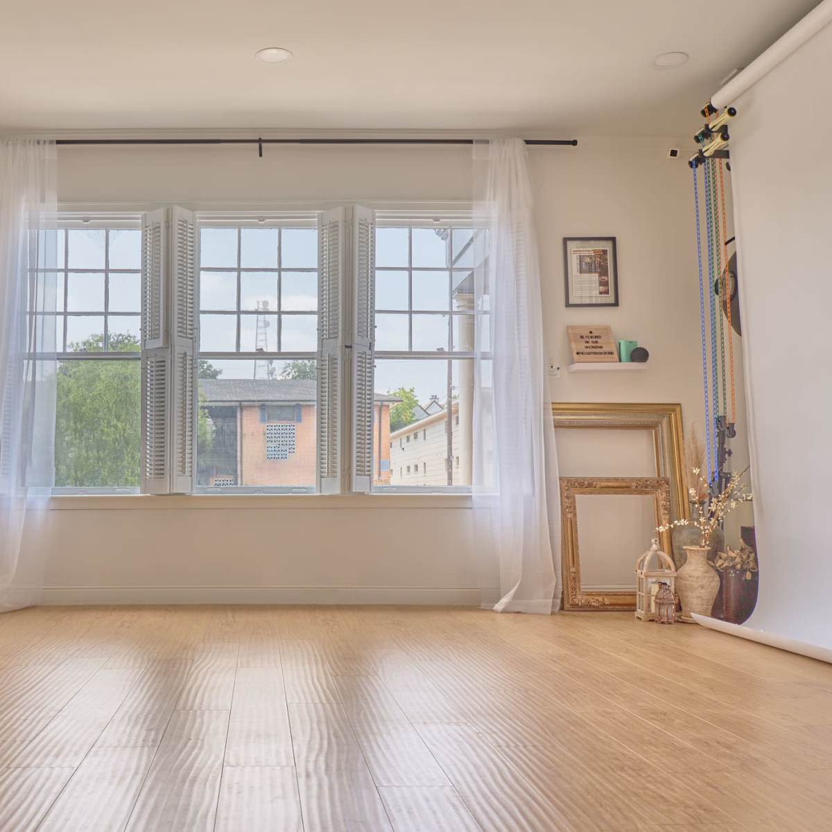 A bright, spacious room with large windows, a decorative mirror, and various framed pictures leaning against the walls.
