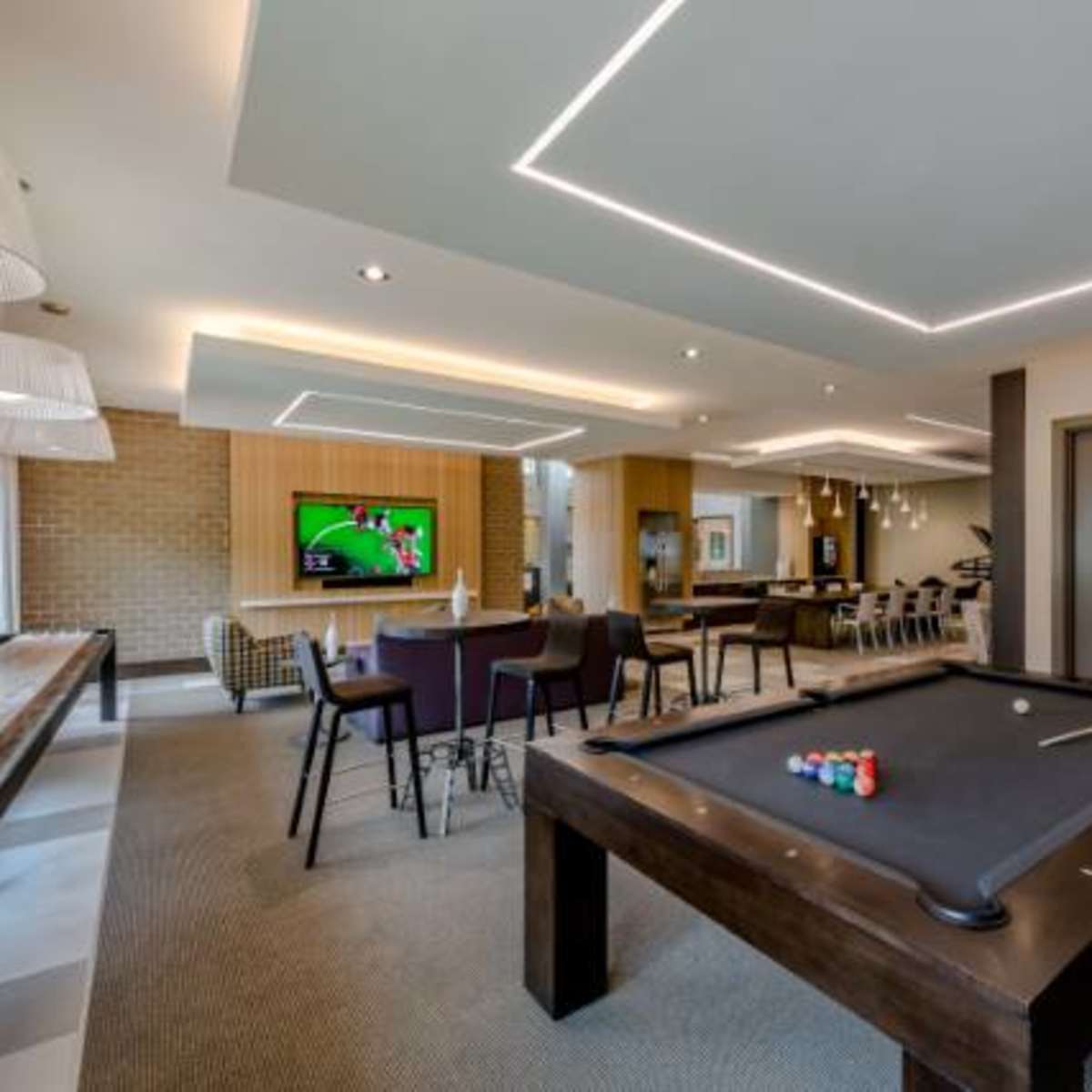 An interior recreational room features a pool table, seating areas, and a large TV on the wall.