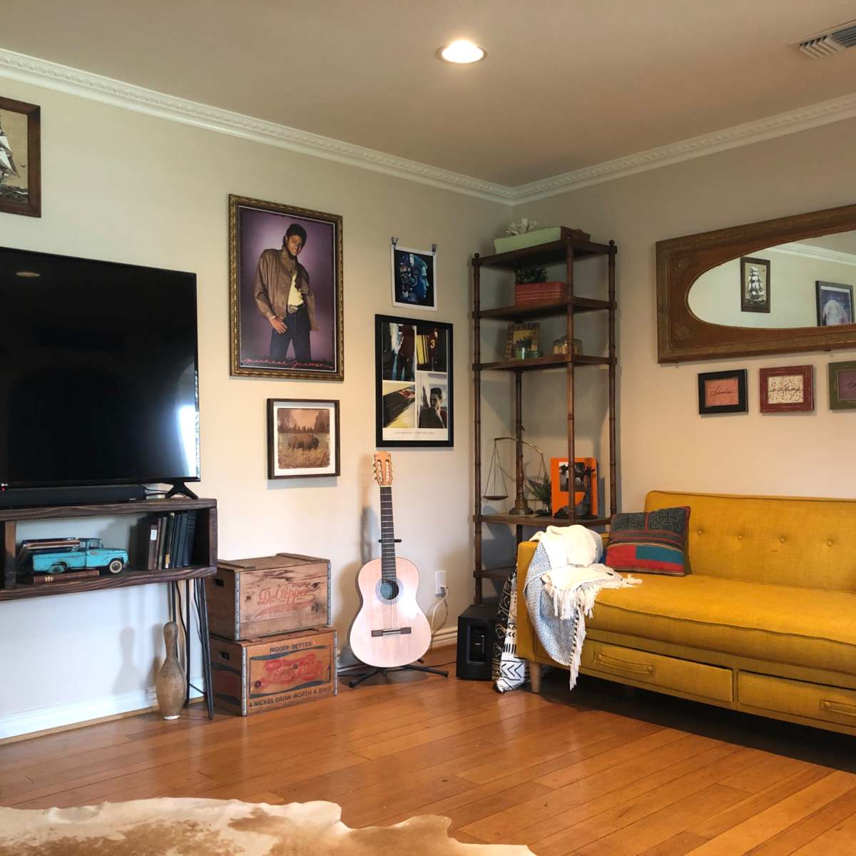 The living room features a yellow sofa, a wooden shelf with decorative items, a television, and various framed pictures on the walls.