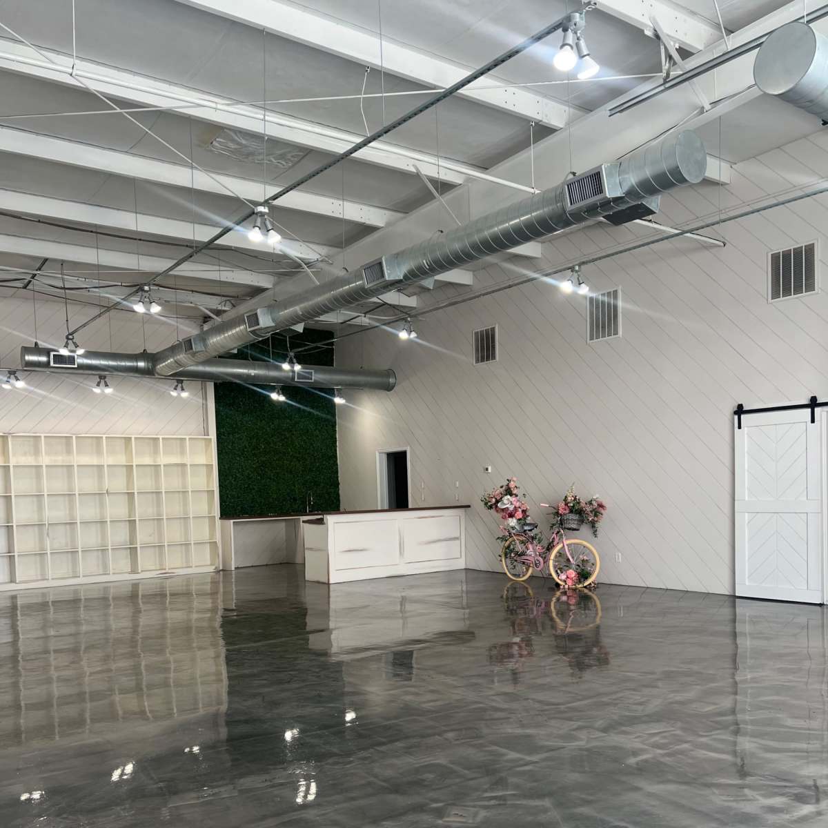 A spacious, empty room with polished concrete floors, a reception area at the back, and decorative bicycles with flowers on either side.