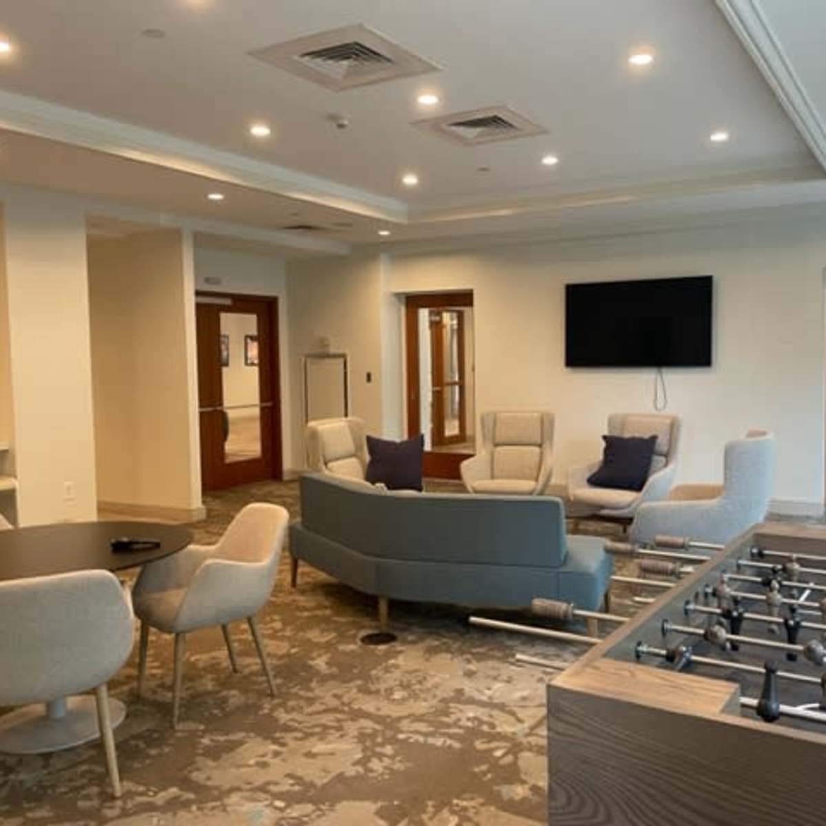 A modern lounge area with seating, a television on the wall, and a foosball table in one corner.