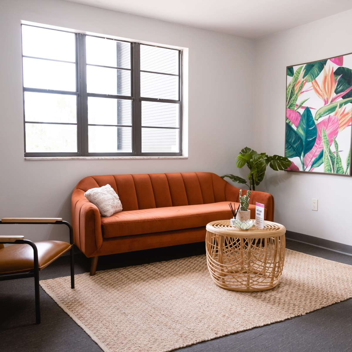 A modern living area features an orange couch, a rattan coffee table, and a large floral artwork on the wall.