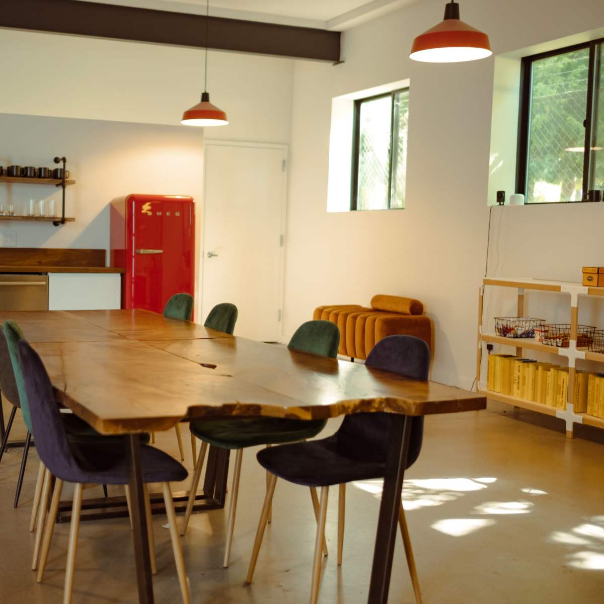 A modern kitchen and dining area featuring a wooden dining table, eight chairs, a red refrigerator, and minimalist decor.