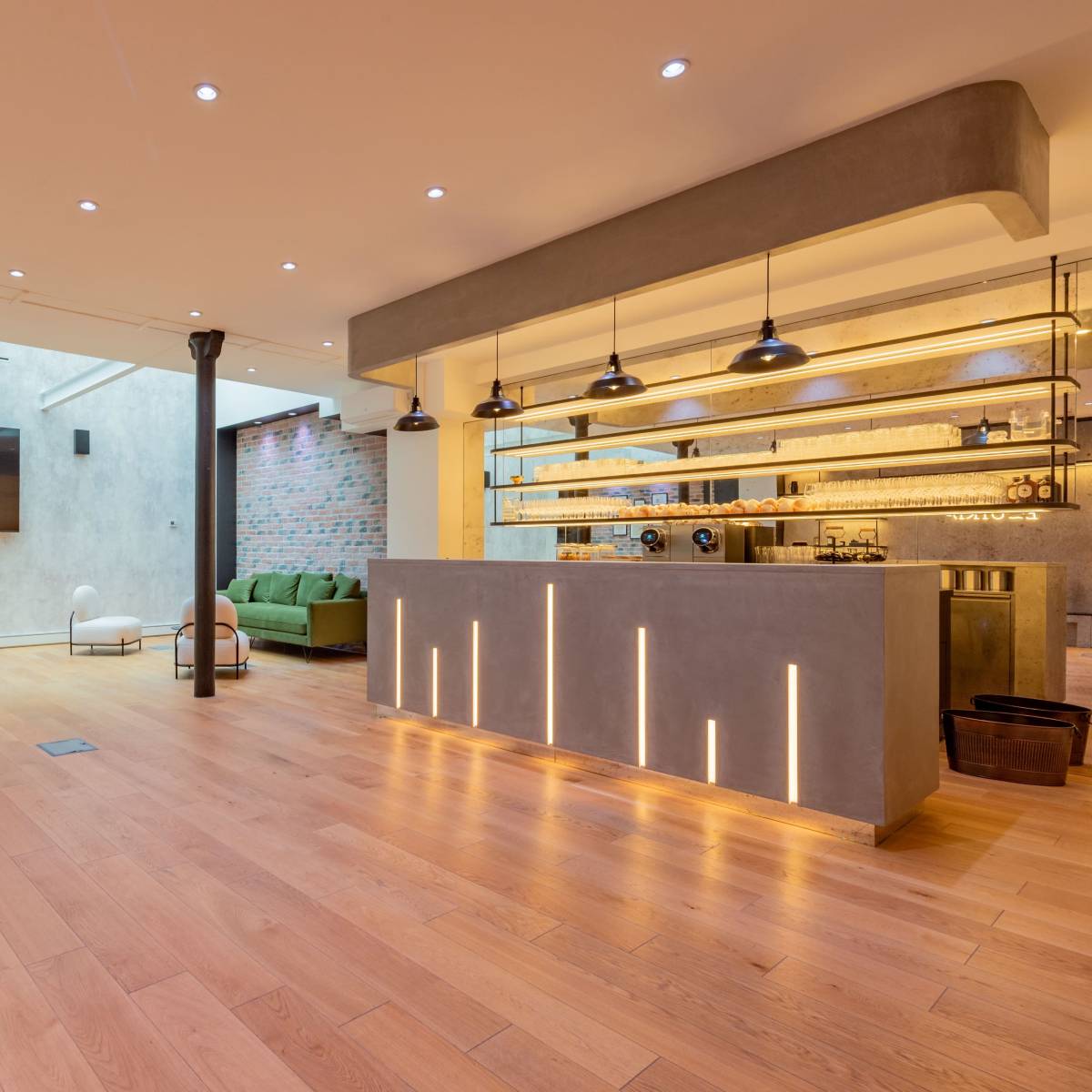 A spacious, modern interior with wooden flooring, a minimalist bar area, and a green seating arrangement against a textured wall.
