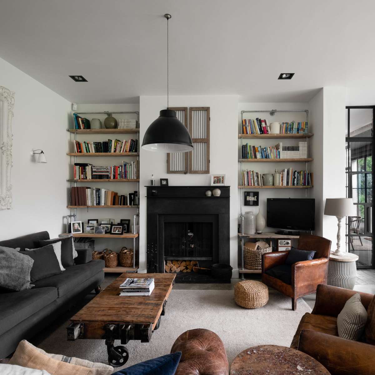 A modern living room with a dark fireplace, bookshelves filled with books, and a mix of comfortable seating arrangements.