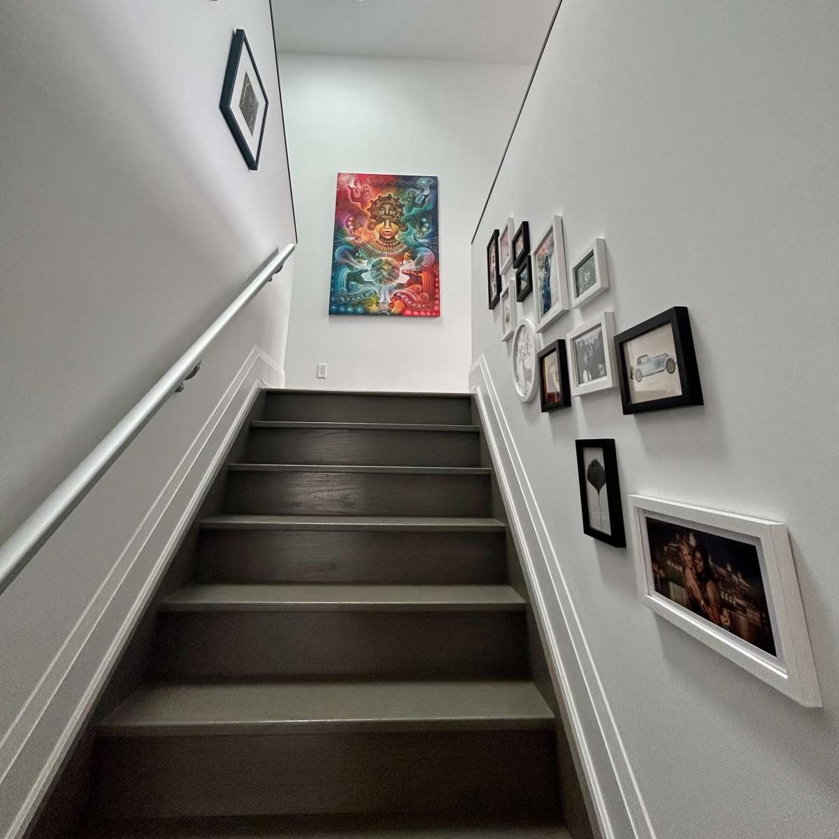 A staircase leads upward, flanked by pictures framed on the wall and a large painting at the top.