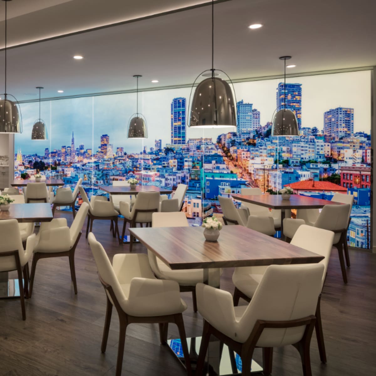 A modern dining area with several tables and chairs, featuring a large wall mural of a city skyline.