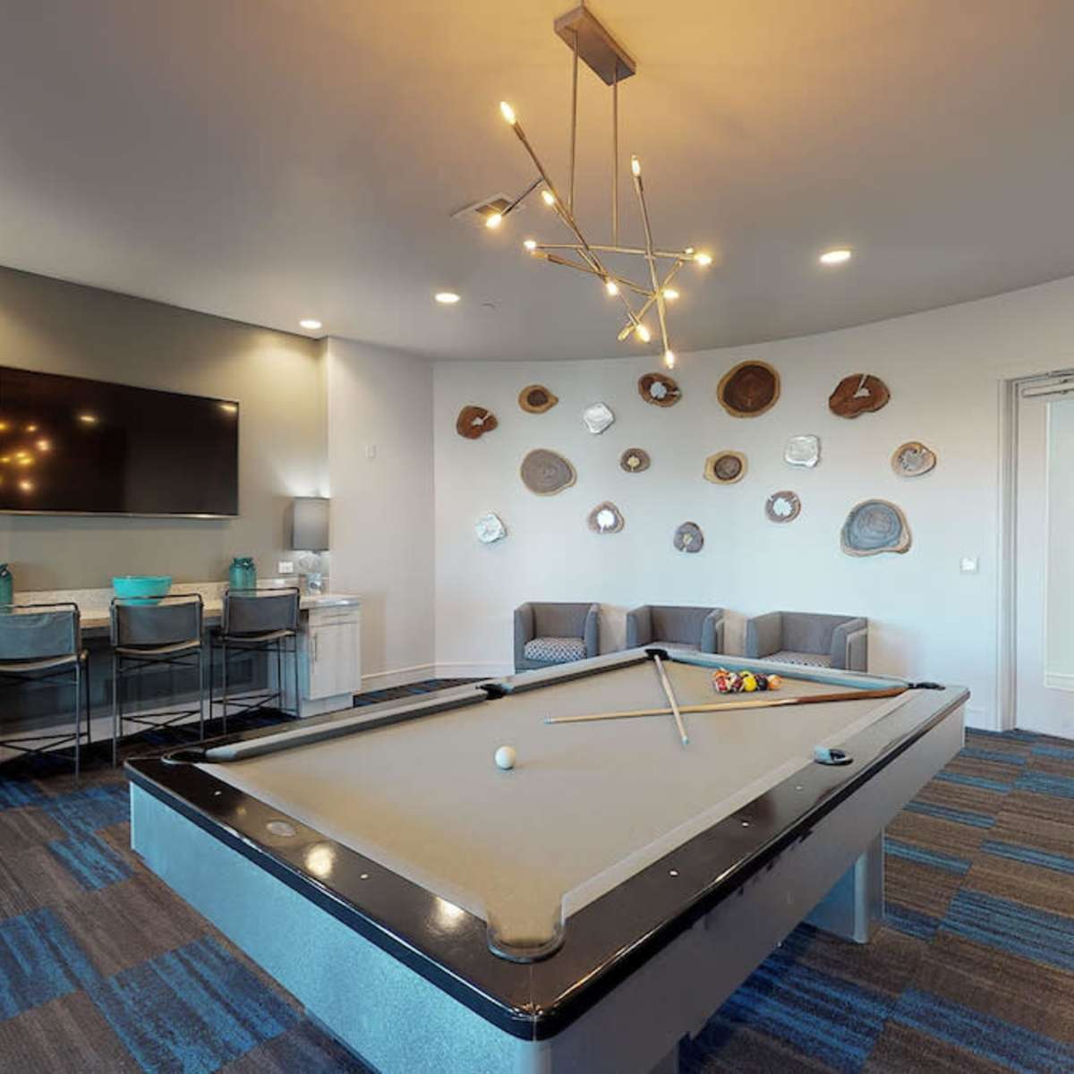 A modern game room featuring a pool table, a large TV, and decorative wall plates, with seating and a small dining area.