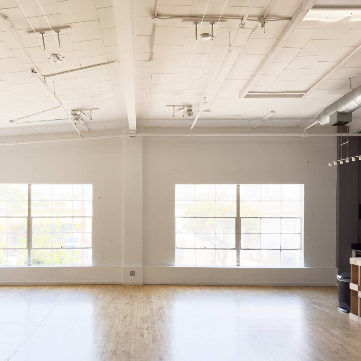 An empty room with wooden flooring and large windows allowing natural light to enter.
