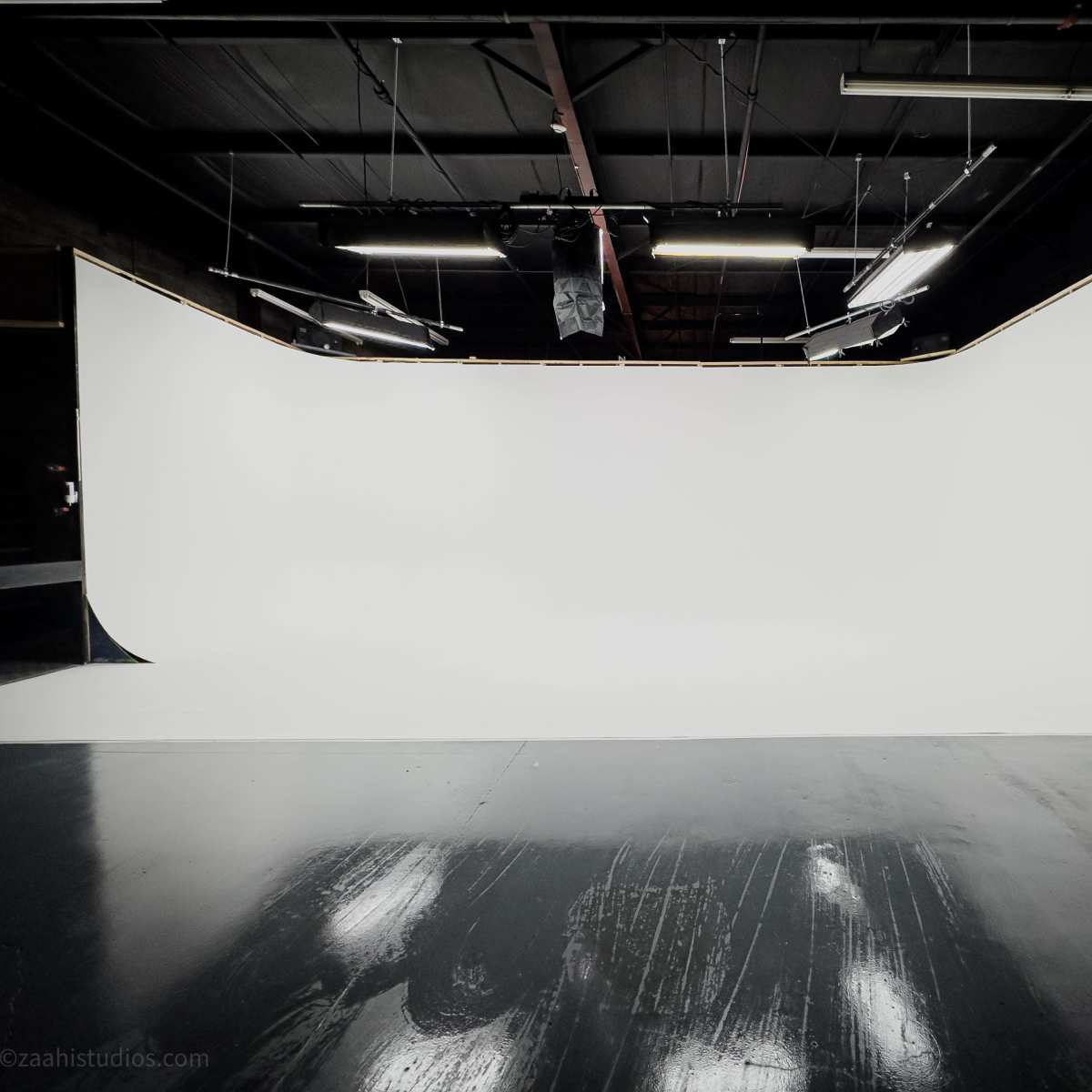 A sleek photography studio features a large, seamless white backdrop and polished black flooring.