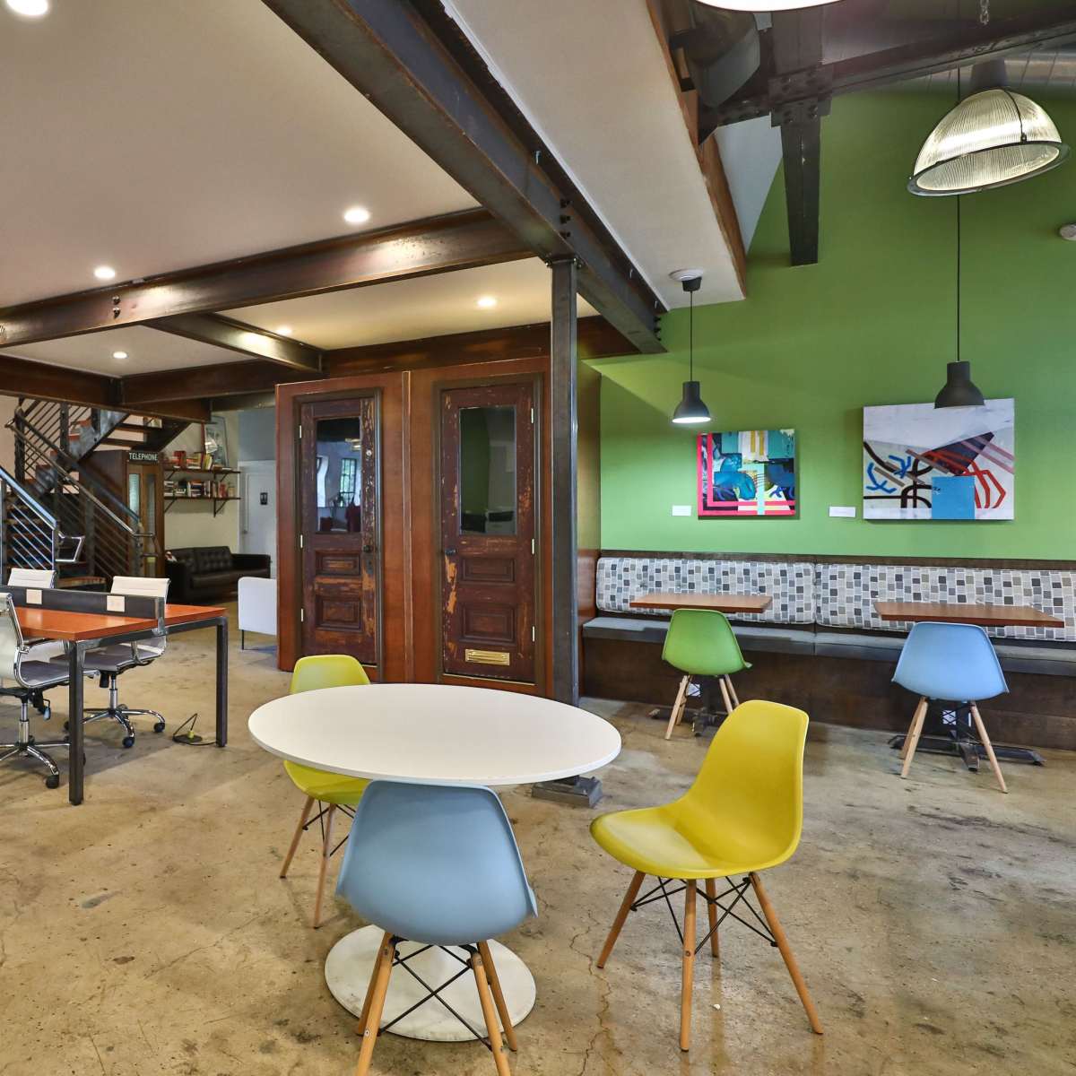 A modern open office space featuring a mix of workstations, seating areas, and colorful chairs against a backdrop of exposed beams and industrial design elements.