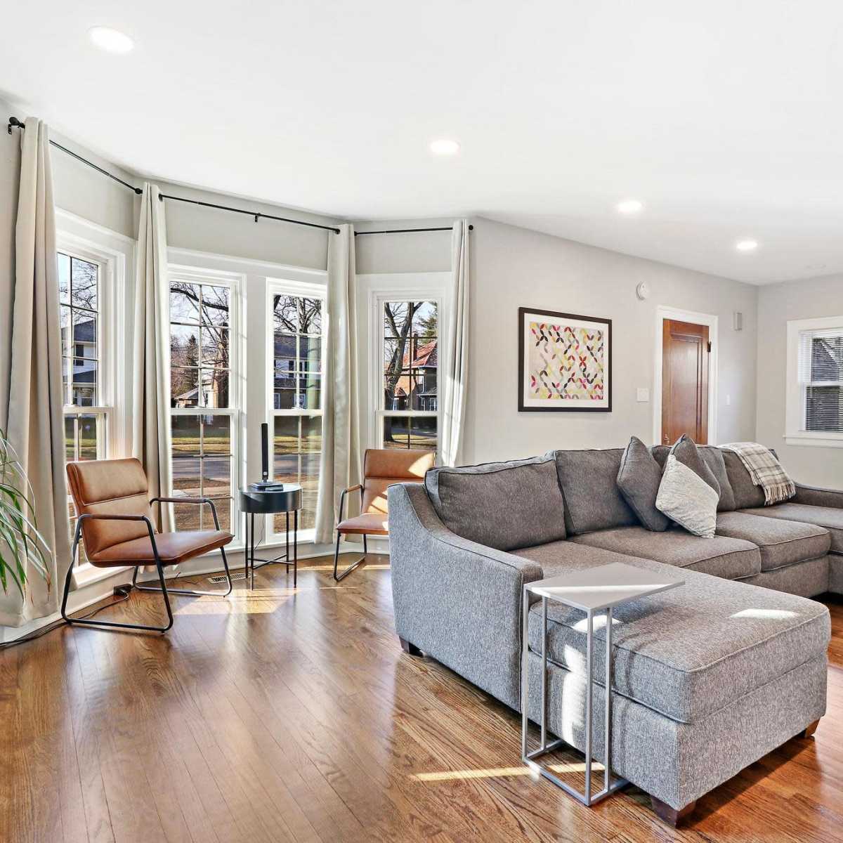 A modern living room with a gray sectional sofa, large windows, and a staircase leading to another level.