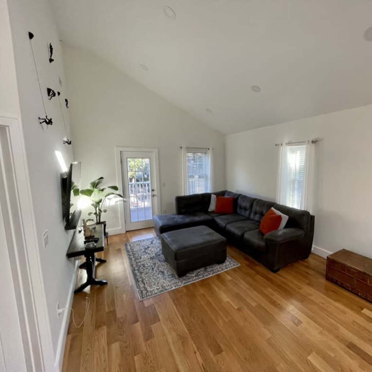 A modern living room features a dark sectional sofa, a wooden coffee table, and large windows allowing natural light.