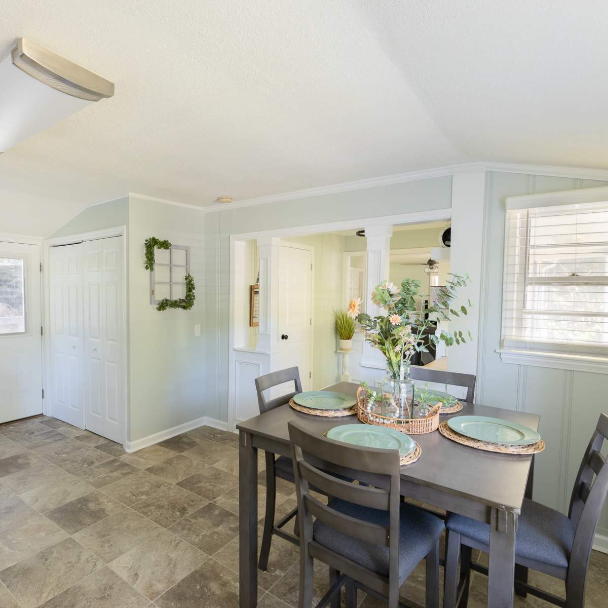 A small dining area with a table set for four is adjacent to a kitchen featuring white cabinetry and a door leading outside.
