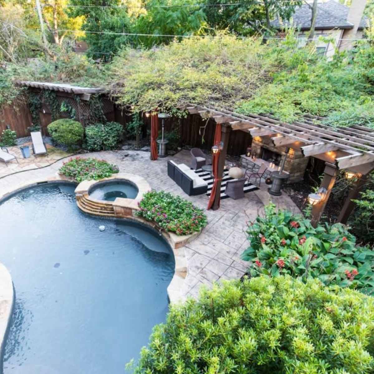 A landscaped backyard with a curved swimming pool surrounded by lounge chairs, a spa, and a pergola.