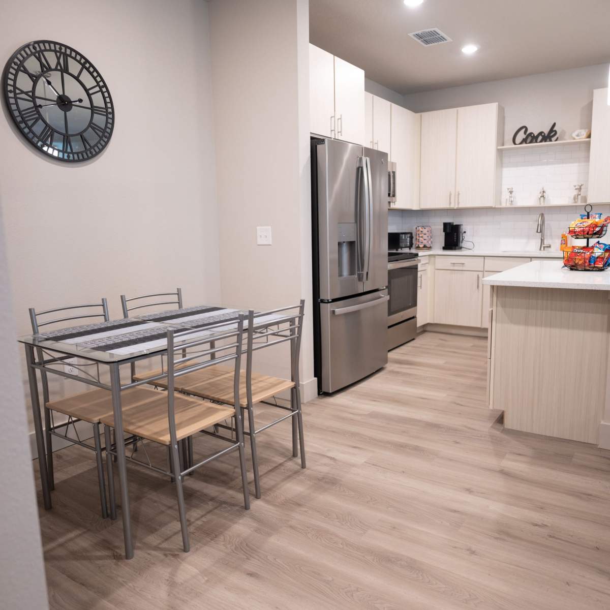 A modern kitchen and dining area with a metal dining table and chairs, stainless steel appliances, and light wood flooring.