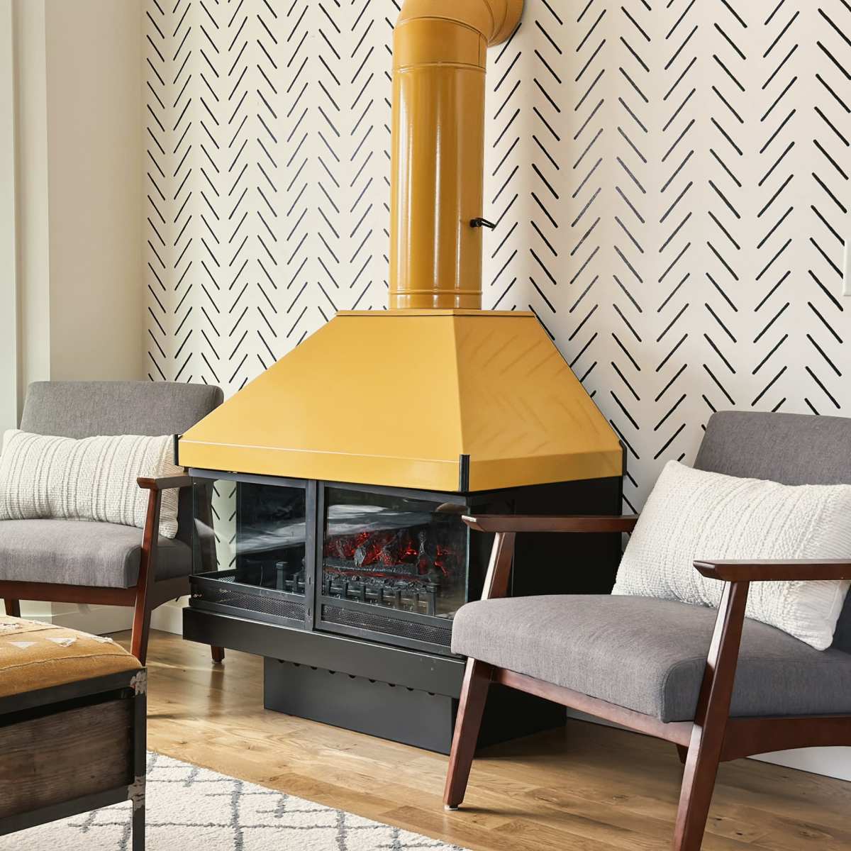 A living room features two gray chairs flanking a yellow triangular fireplace, with a patterned wall and a window revealing an outdoor view.