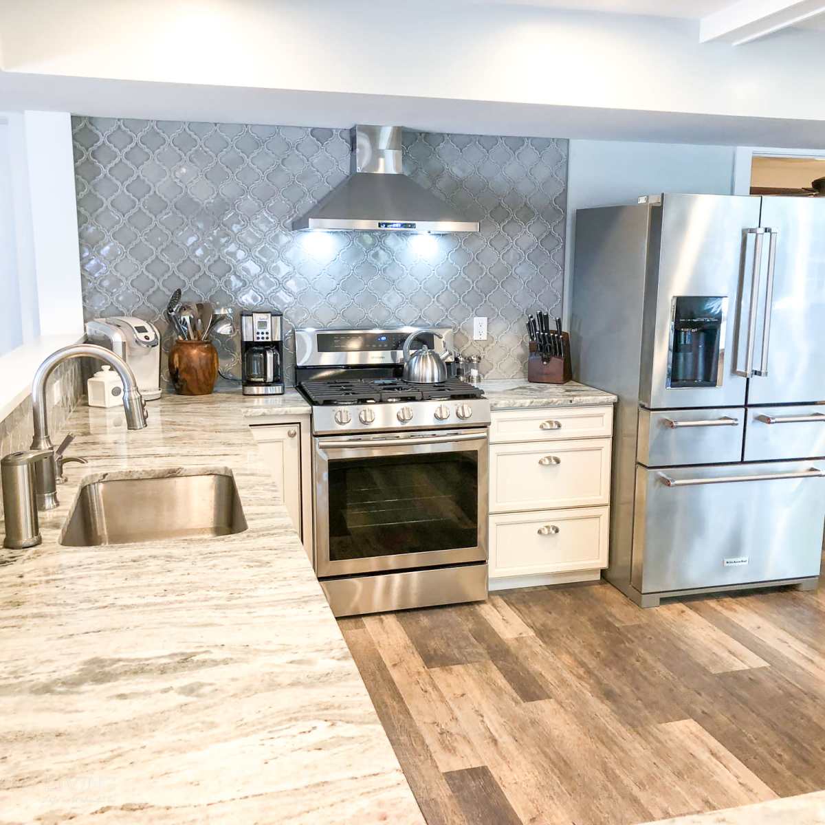 A modern kitchen featuring stainless steel appliances, including a stove and refrigerator, with a light-colored countertop and a backsplash of patterned tiles.