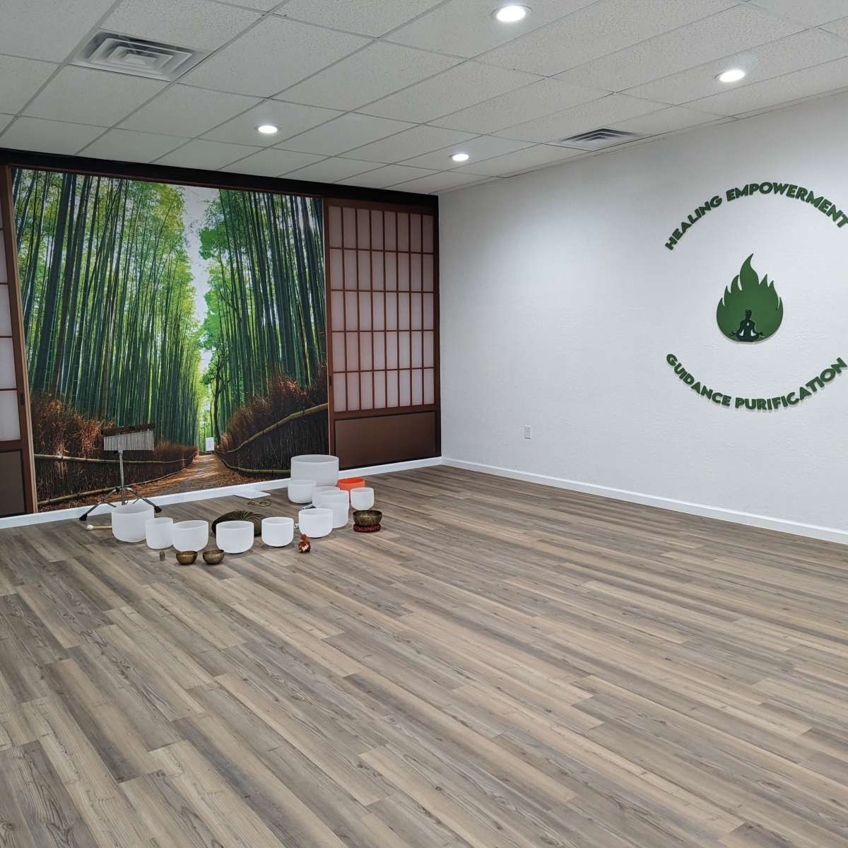 A spacious room with bamboo wall art, wooden flooring, and various sound healing bowls arranged on the floor.