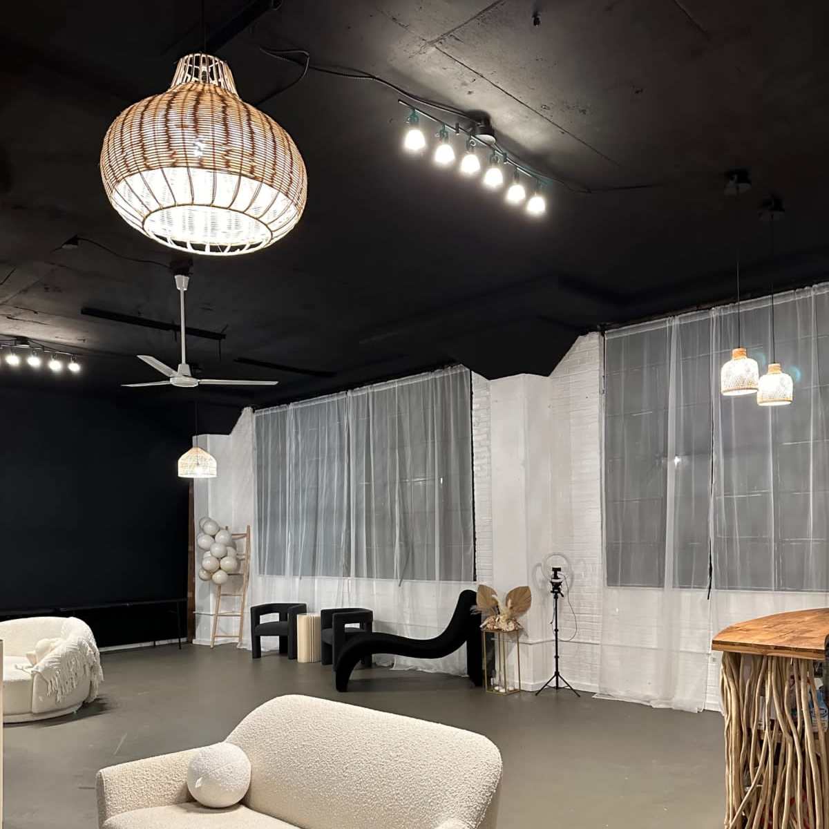 A spacious, minimalist room with a light-colored sofa, a large wooden table, and various pendant lights hanging from the ceiling.