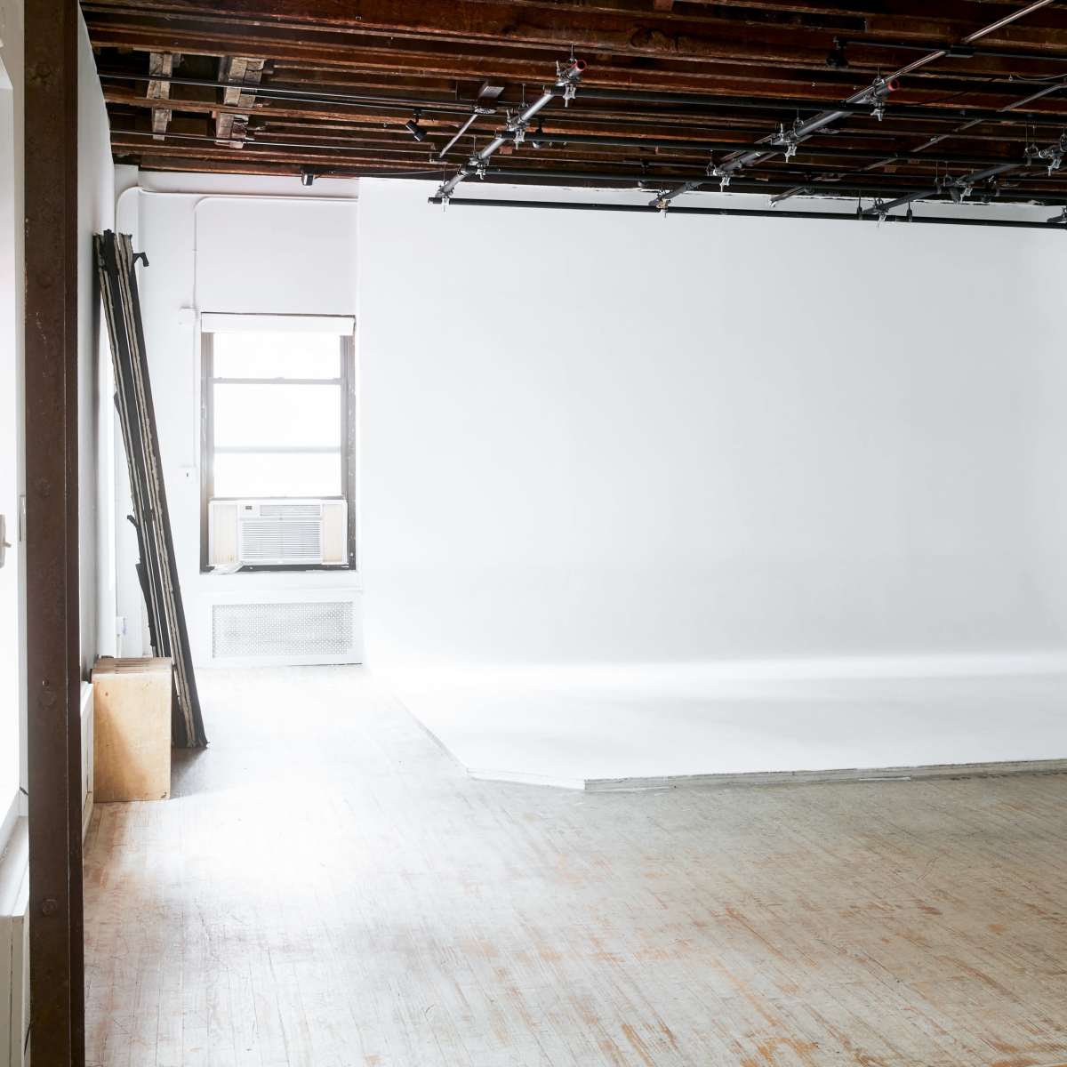A spacious photography studio with a large white backdrop and wooden flooring.