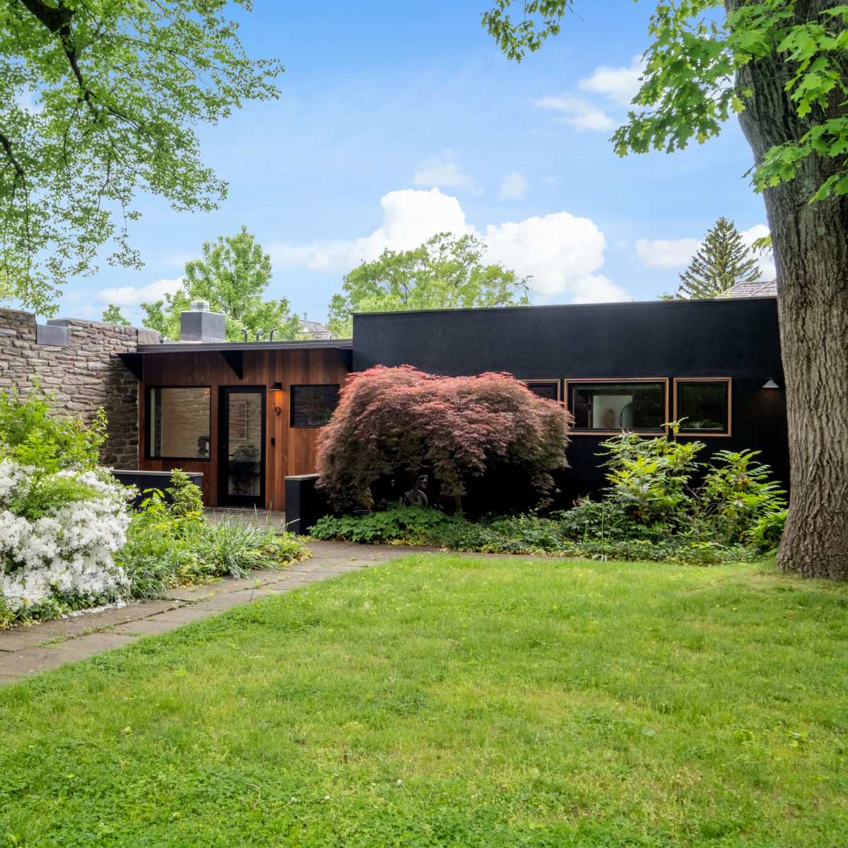 A modern house with a stone wall and landscaped garden featuring various plants and flowers lines a stone pathway.