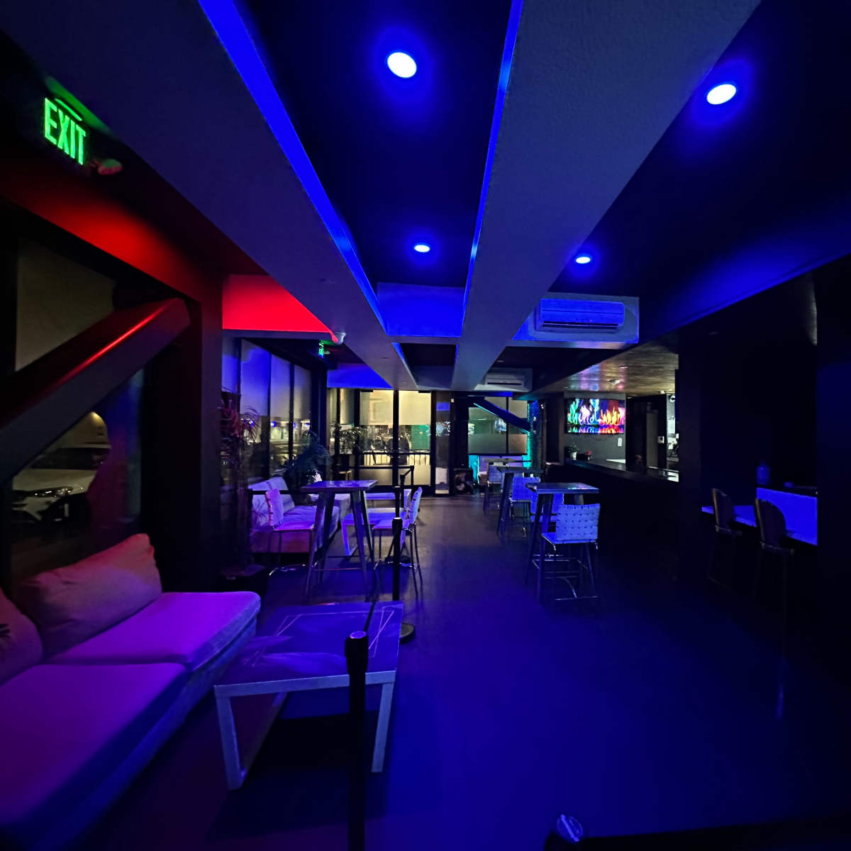 A dimly lit lounge features blue and red lighting, with seating areas and a bar visible in the background.