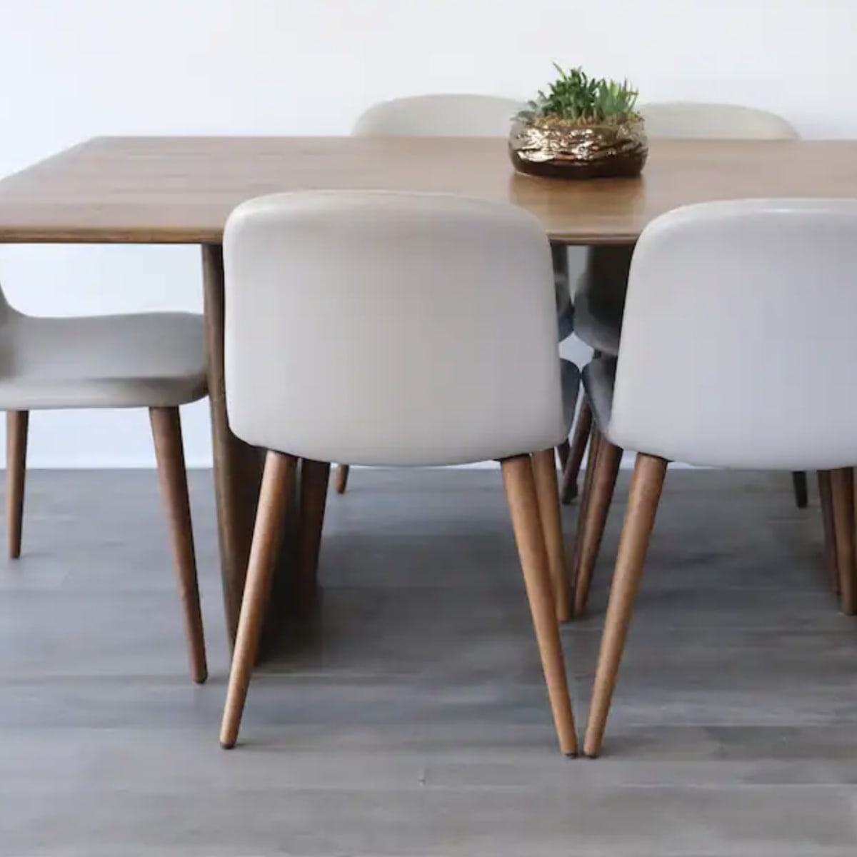A wooden dining table is surrounded by five light-colored chairs with wooden legs, and a small decorative plant sits in the center.