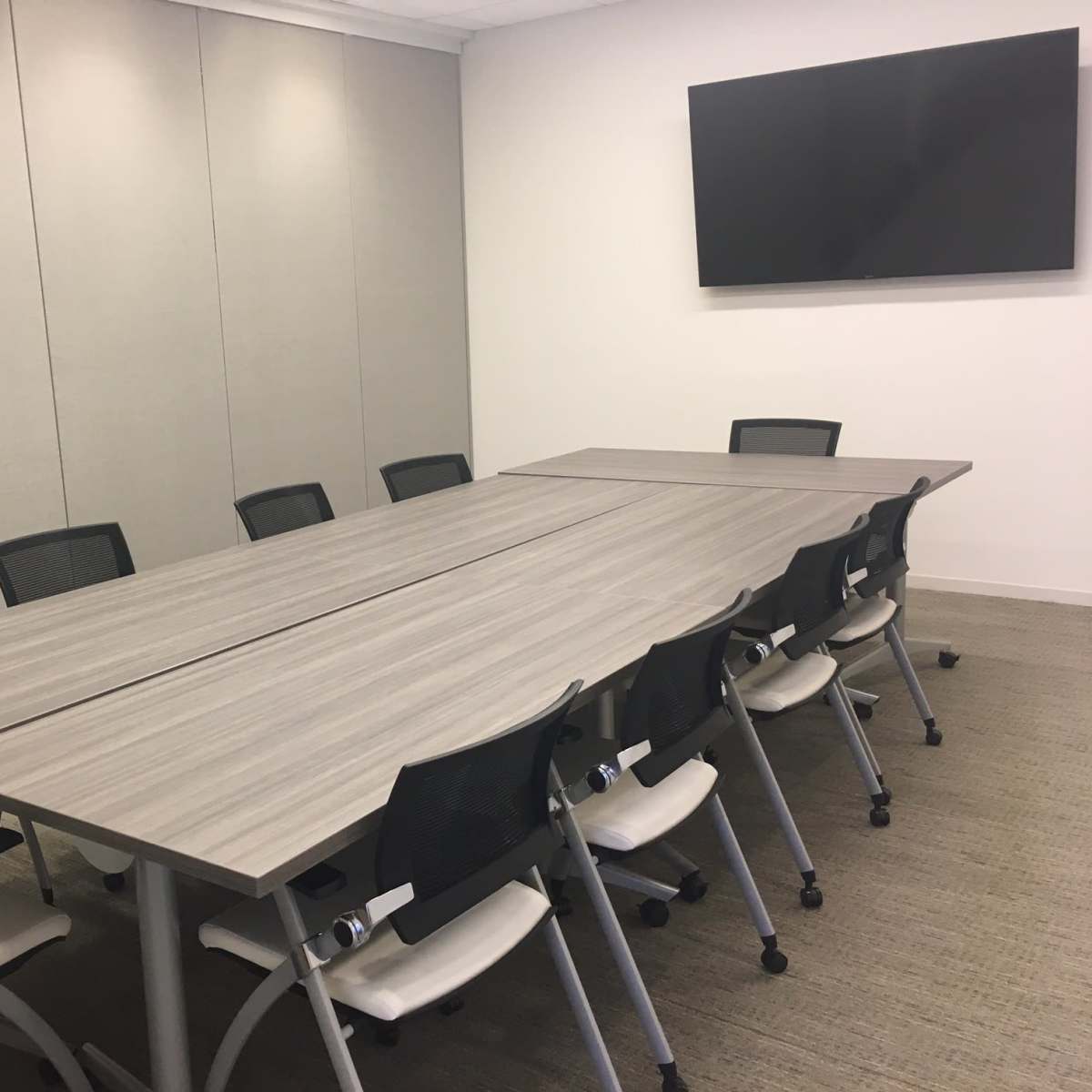 A large conference room features a long rectangular table with ten ergonomic chairs and a wall-mounted flat-screen television.