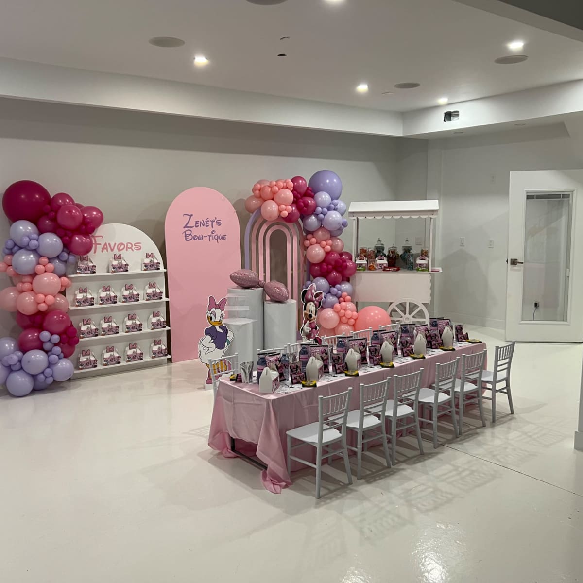 A decorated party room with a table set for a celebration, featuring balloons, a display of favors, and themed decorations.