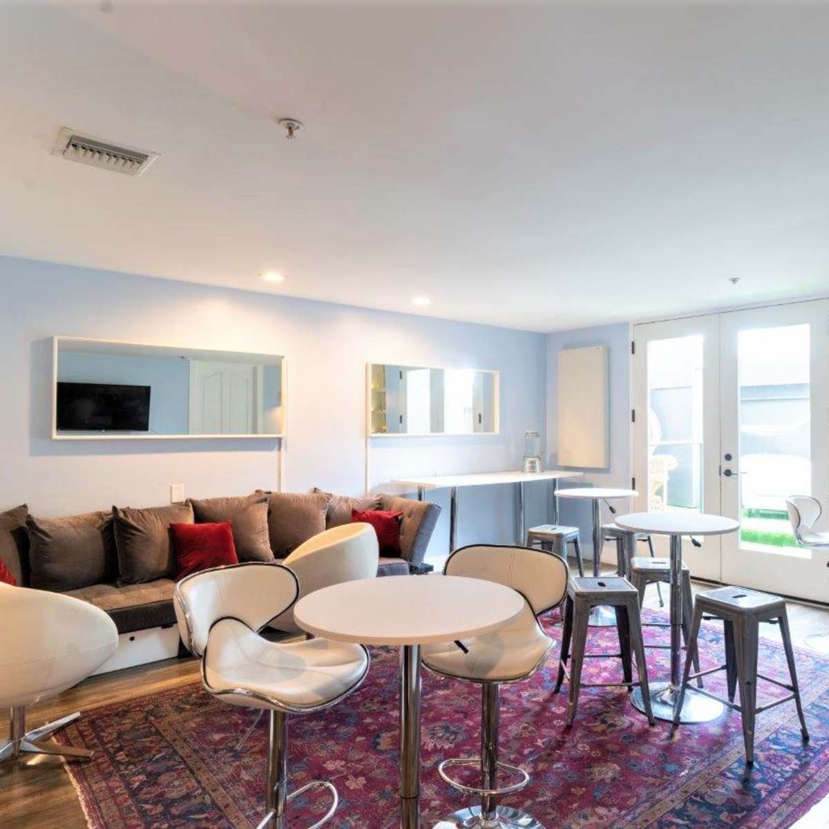 A modern lounge area with a large sofa, several round tables, and a bar setup, featuring glass doors that lead to an outdoor space.