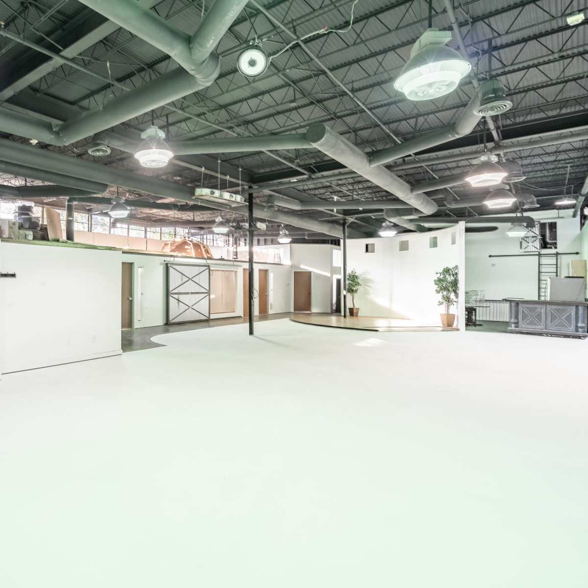 A spacious, well-lit industrial room with high ceilings, exposed ducts, and minimal furnishings.