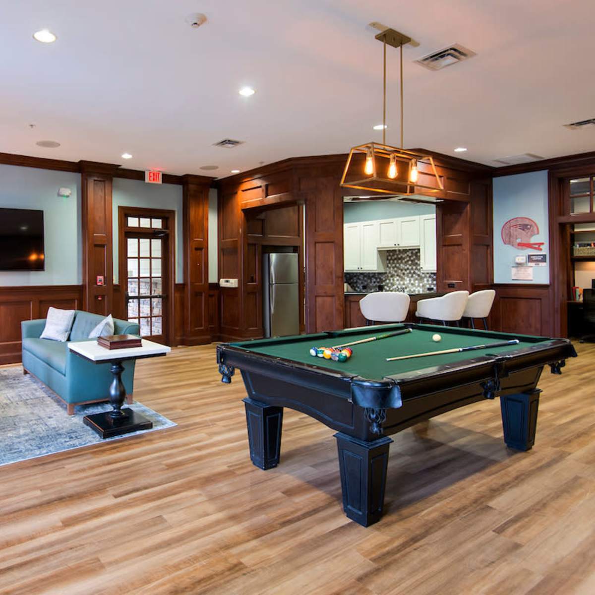 A modern lounge area featuring a pool table, a television on the wall, and seating arranged around a wooden interior with large windows.