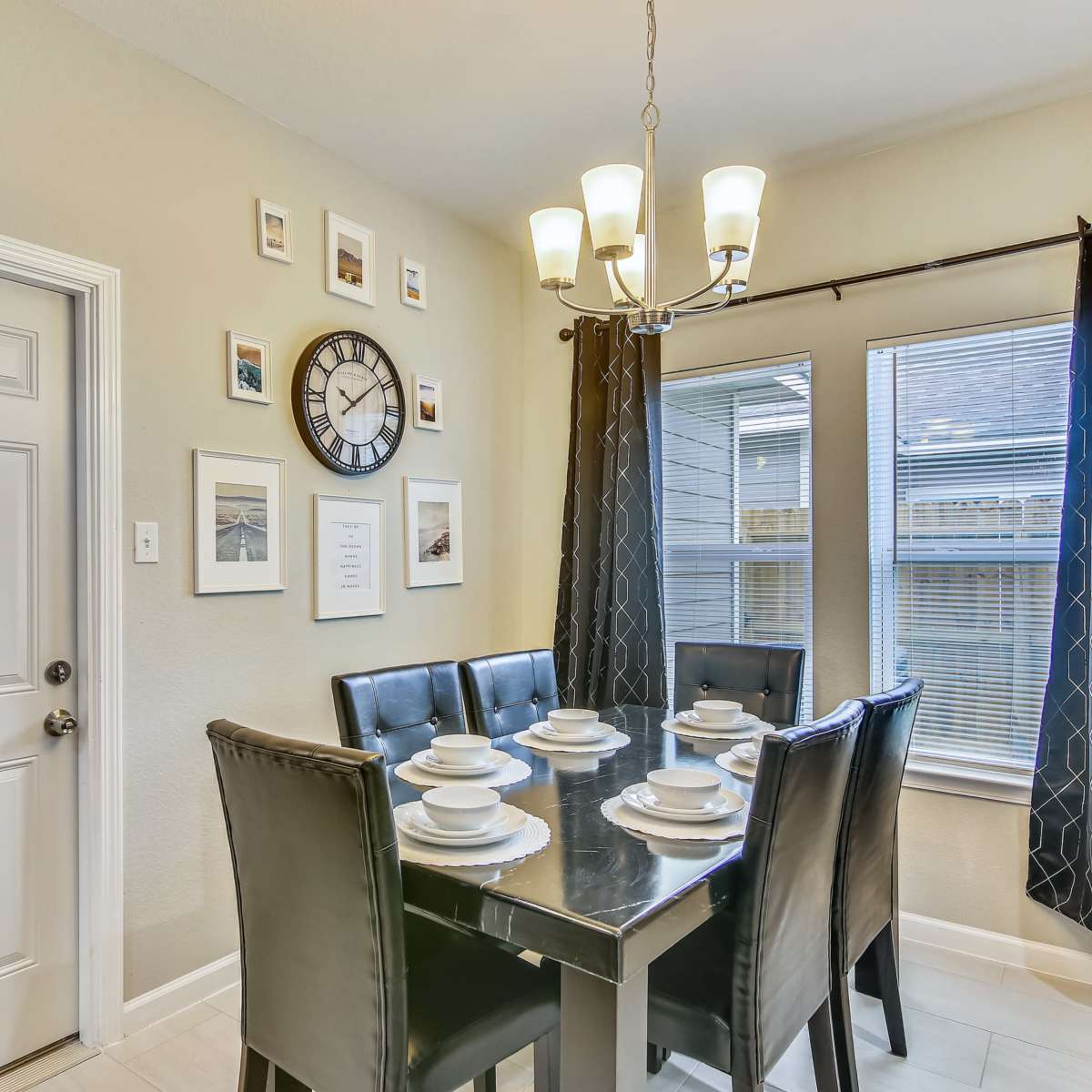 A dining area features a black table set for six, surrounded by leather chairs, with a clock and framed pictures on the wall.
