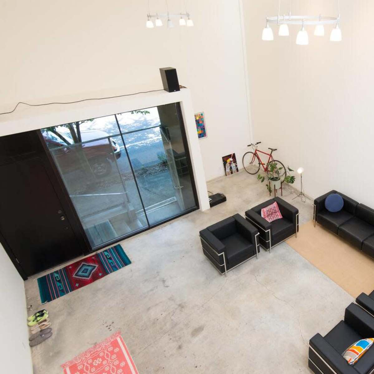 A modern, spacious living area with concrete flooring, black leather furniture, and large windows allowing natural light.